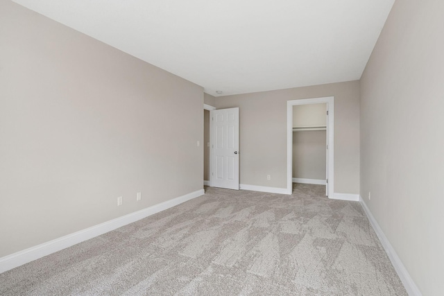 unfurnished bedroom with a closet, a walk in closet, light colored carpet, and baseboards