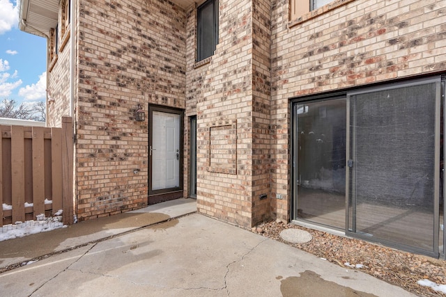 view of exterior entry featuring brick siding and fence