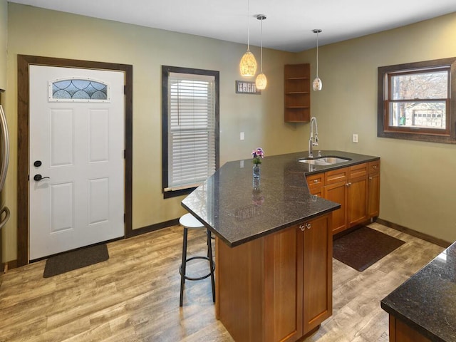 kitchen with light wood finished floors, brown cabinets, decorative light fixtures, a peninsula, and a sink