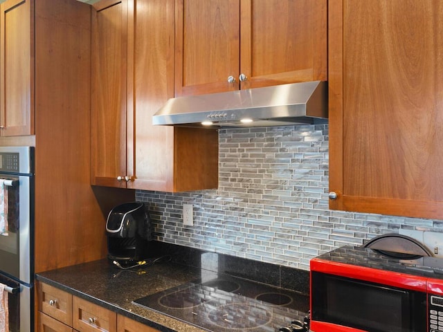 kitchen featuring double oven, black electric stovetop, under cabinet range hood, backsplash, and brown cabinets