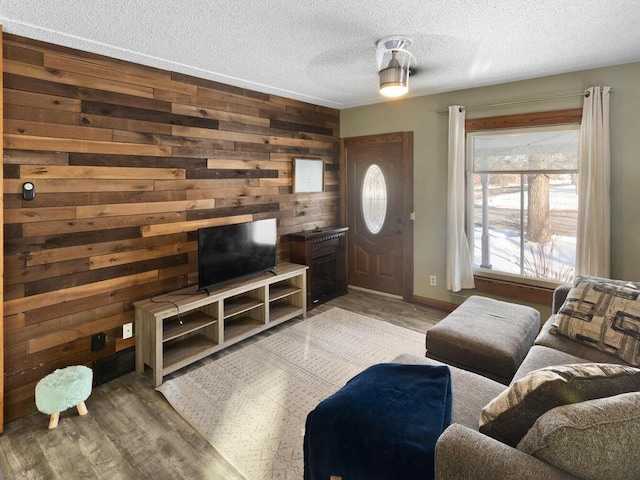 living area featuring wood walls, a textured ceiling, baseboards, and wood finished floors