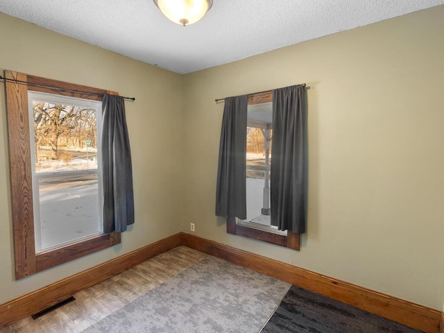 empty room featuring visible vents, plenty of natural light, baseboards, and wood finished floors