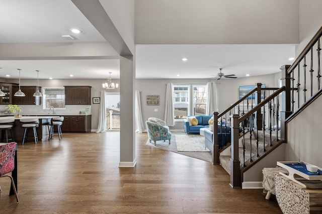 living room featuring recessed lighting, ceiling fan with notable chandelier, dark wood-style flooring, baseboards, and stairway