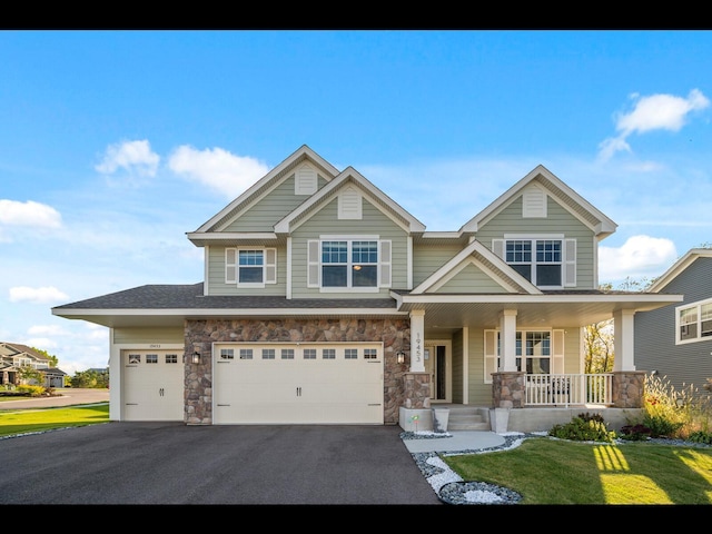 craftsman-style home featuring driveway, stone siding, a porch, an attached garage, and a front lawn