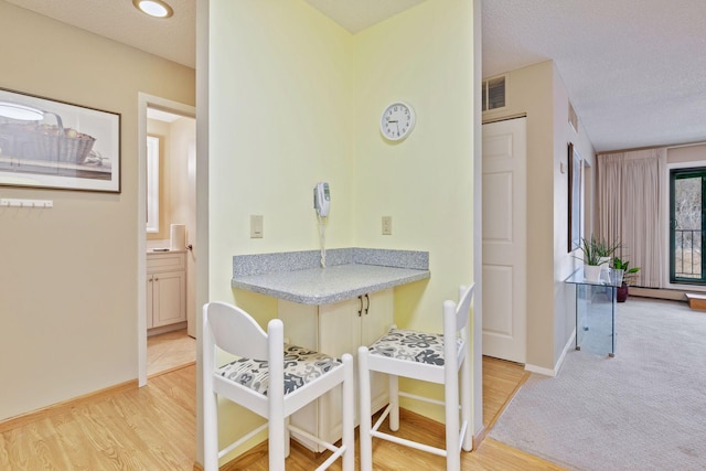 dining space with baseboards, visible vents, light wood-style flooring, a textured ceiling, and light colored carpet