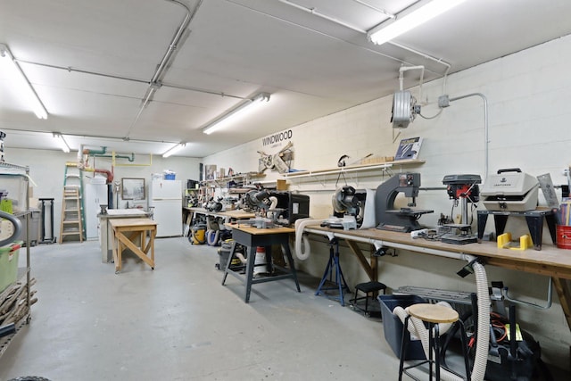 garage featuring a workshop area, concrete block wall, and freestanding refrigerator