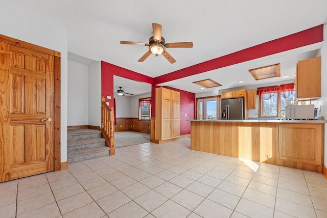 kitchen featuring stainless steel refrigerator with ice dispenser, a textured ceiling, a peninsula, light tile patterned floors, and ceiling fan