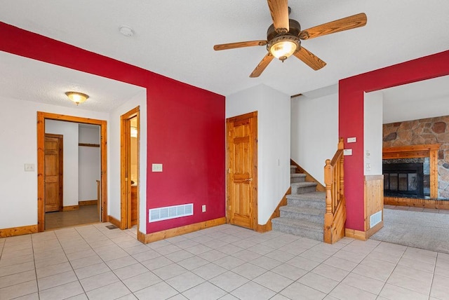 unfurnished room with visible vents, a stone fireplace, ceiling fan, and stairway