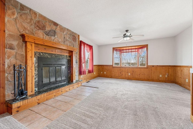 unfurnished living room with carpet floors, wainscoting, a fireplace, a textured ceiling, and a ceiling fan