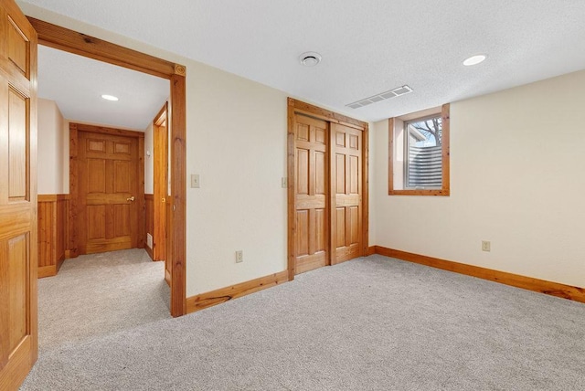 unfurnished bedroom with baseboards, visible vents, a closet, a textured ceiling, and light colored carpet