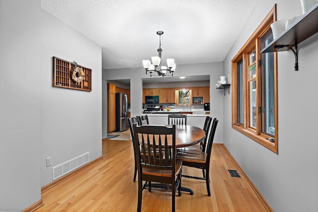 dining area featuring a notable chandelier, visible vents, light wood-style floors, a textured ceiling, and baseboards