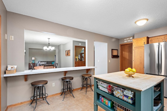 kitchen with a breakfast bar area, open shelves, light countertops, freestanding refrigerator, and baseboards