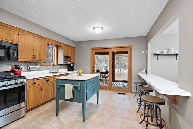 kitchen with black microwave, a sink, plenty of natural light, light countertops, and gas stove