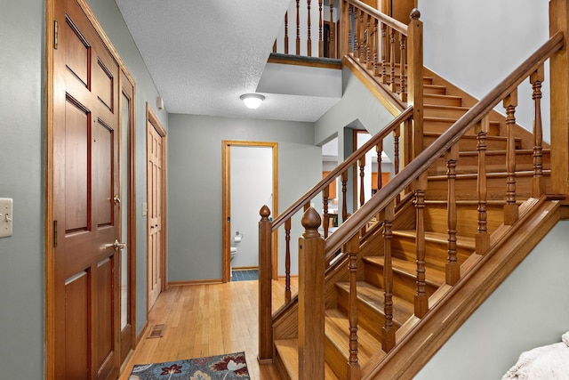 staircase featuring wood-type flooring, a textured ceiling, and baseboards