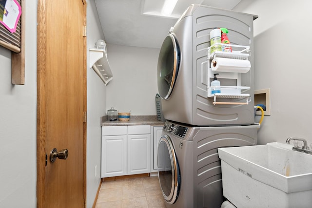 washroom featuring stacked washer and clothes dryer, cabinet space, a sink, and light tile patterned floors