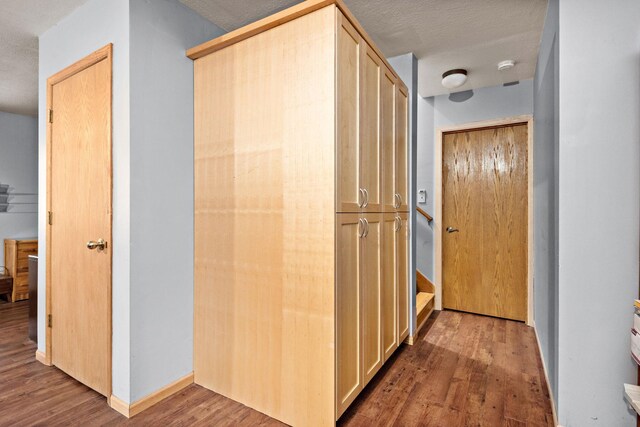 hall featuring a textured ceiling, wood finished floors, and baseboards