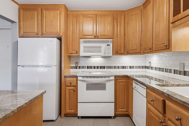 kitchen with light stone counters, tasteful backsplash, brown cabinetry, light tile patterned flooring, and white appliances