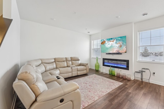 living area featuring dark wood-type flooring, a glass covered fireplace, and baseboards