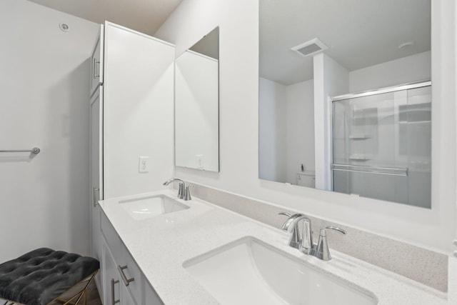 bathroom with double vanity, an enclosed shower, a sink, and visible vents