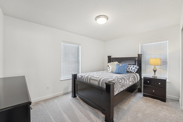 bedroom featuring light carpet, multiple windows, a textured ceiling, and baseboards