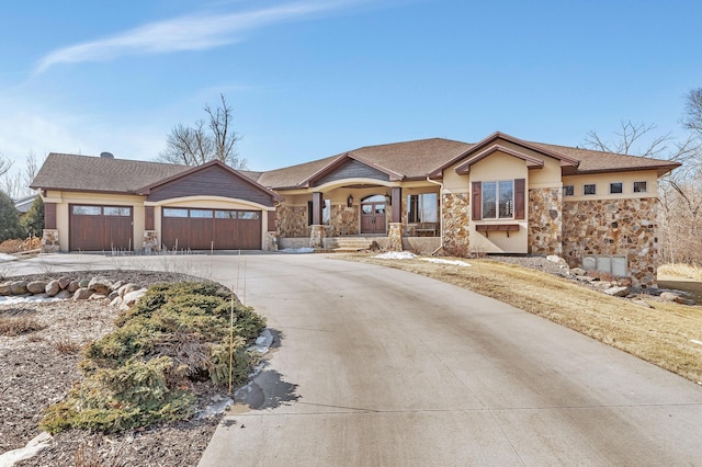 view of front of property with a garage, stone siding, driveway, and stucco siding