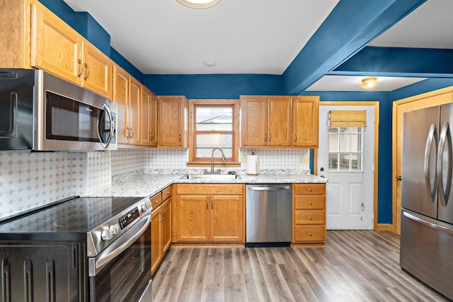 kitchen featuring light stone counters, stainless steel appliances, tasteful backsplash, a sink, and light wood-type flooring