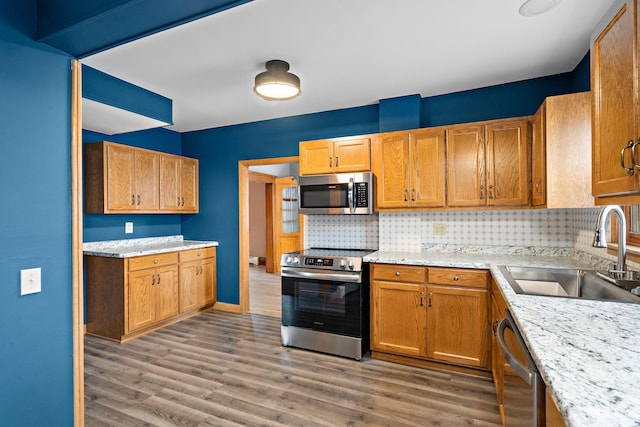 kitchen featuring stainless steel appliances, wood finished floors, backsplash, and a sink