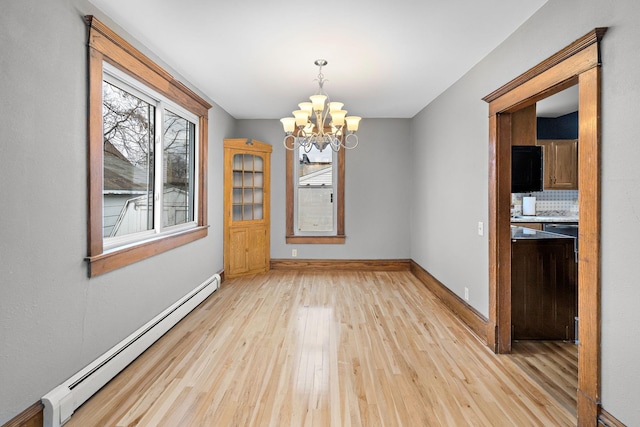 unfurnished dining area featuring light wood-type flooring, plenty of natural light, baseboard heating, and a notable chandelier