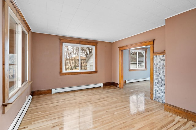 spare room featuring a baseboard heating unit, light wood-type flooring, and baseboards