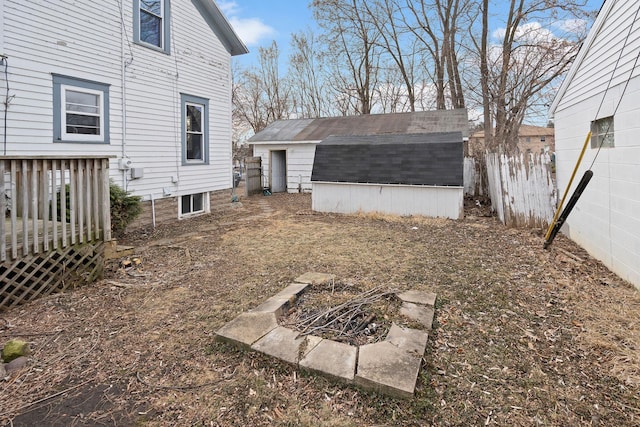 view of yard with a fire pit, fence, a deck, an outdoor structure, and a shed