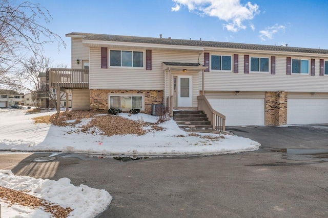 raised ranch with central air condition unit, brick siding, an attached garage, and driveway