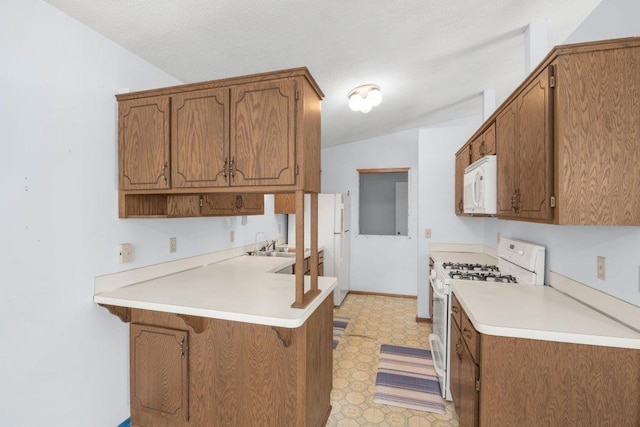 kitchen featuring light floors, a breakfast bar area, brown cabinets, a peninsula, and white appliances