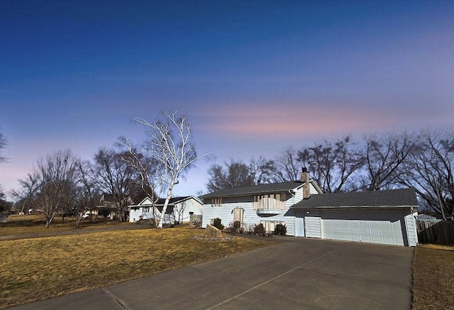 view of front facade featuring concrete driveway, a chimney, an attached garage, and a front yard