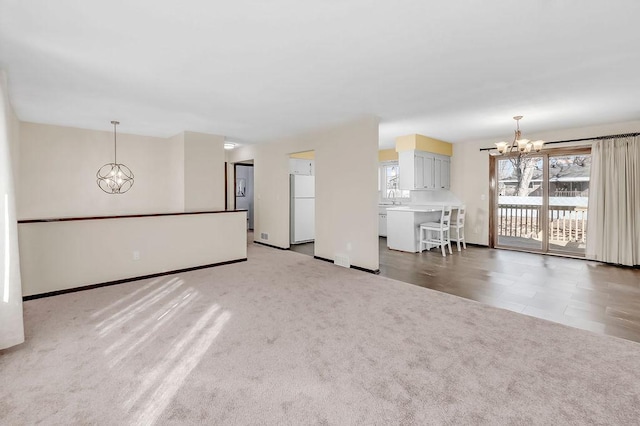 unfurnished living room featuring carpet floors, a sink, visible vents, baseboards, and an inviting chandelier