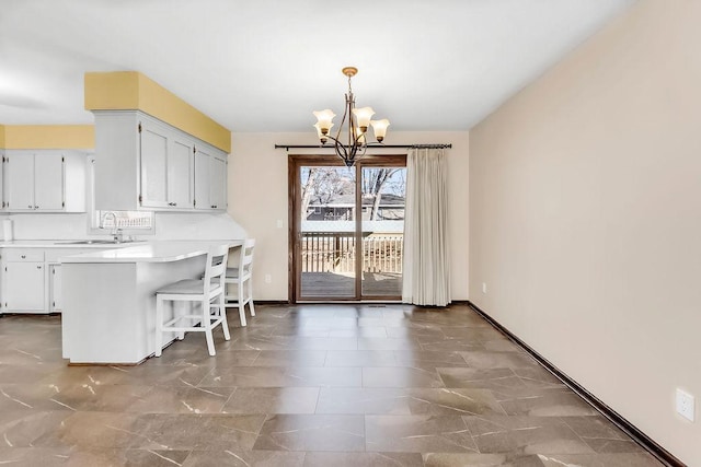 kitchen featuring a breakfast bar area, light countertops, an inviting chandelier, a sink, and a peninsula