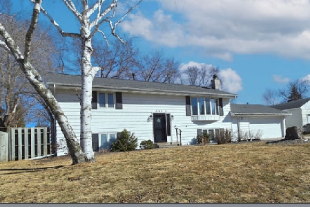 raised ranch with a front lawn, a chimney, and fence