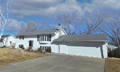 raised ranch featuring an attached garage, a chimney, fence, and concrete driveway