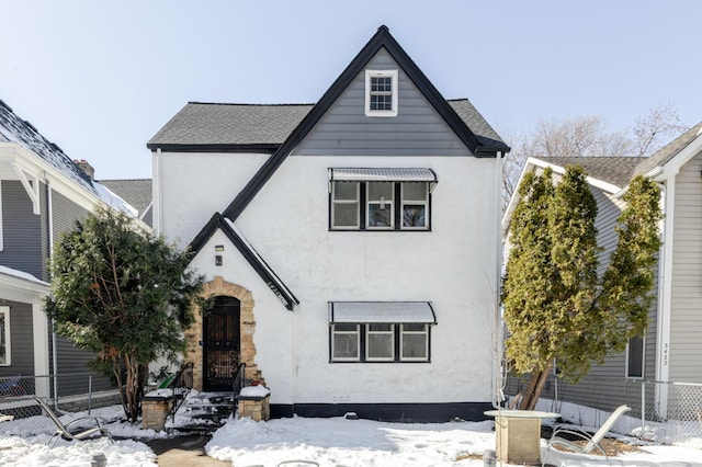 tudor house with stucco siding, a shingled roof, and fence