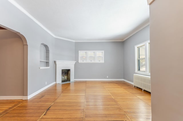 unfurnished living room featuring a fireplace with flush hearth, built in shelves, radiator heating unit, arched walkways, and baseboards