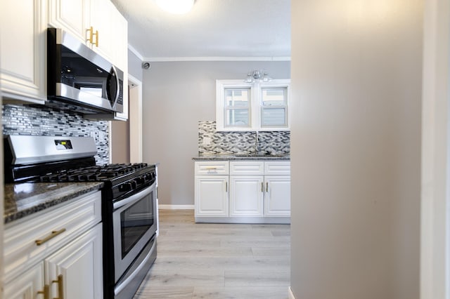 kitchen featuring light wood-style flooring, a sink, dark stone counters, appliances with stainless steel finishes, and white cabinets