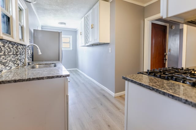 kitchen with white cabinets, a textured ceiling, baseboards, and a sink