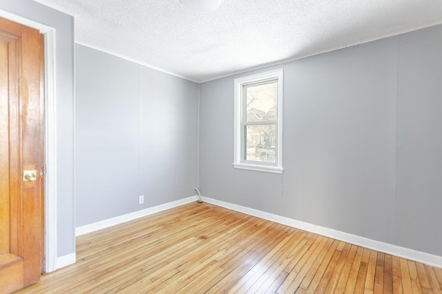 empty room featuring light wood-style flooring, a textured ceiling, baseboards, and ornamental molding