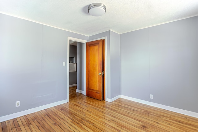 unfurnished room with light wood-style flooring, a textured ceiling, baseboards, and ornamental molding