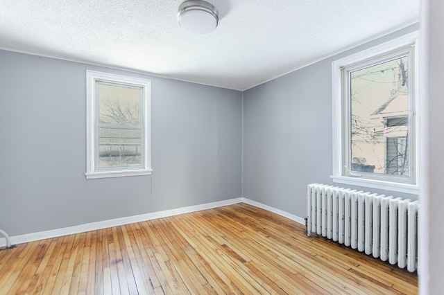 spare room featuring hardwood / wood-style floors, radiator, baseboards, and a textured ceiling