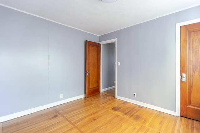 empty room featuring ornamental molding, light wood-style floors, baseboards, and a textured ceiling