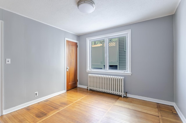 unfurnished room featuring radiator, a textured ceiling, baseboards, and wood finished floors