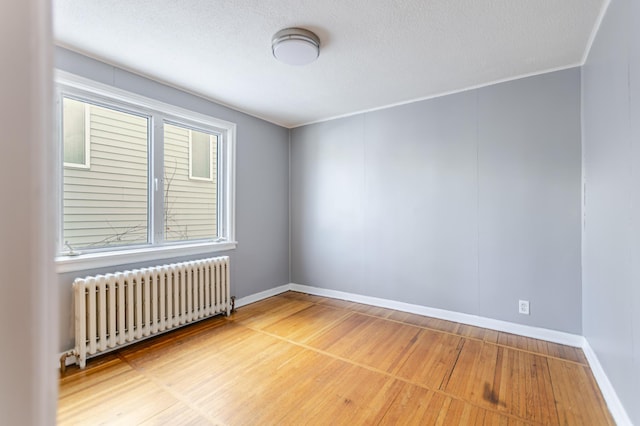 unfurnished room featuring radiator heating unit, wood finished floors, baseboards, and a textured ceiling