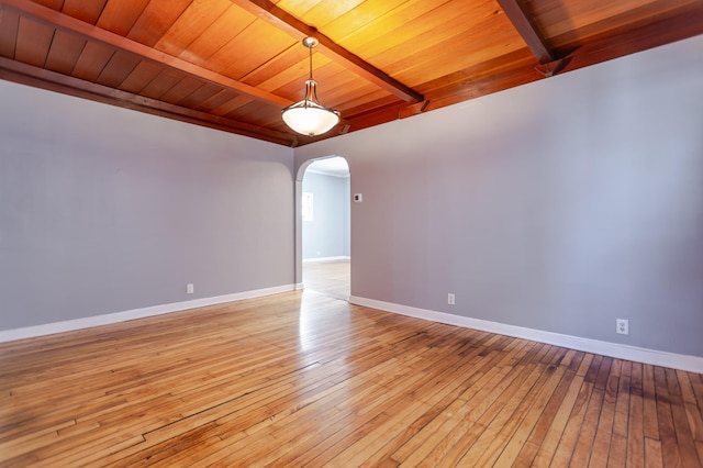 spare room featuring beamed ceiling, baseboards, arched walkways, and light wood-style flooring