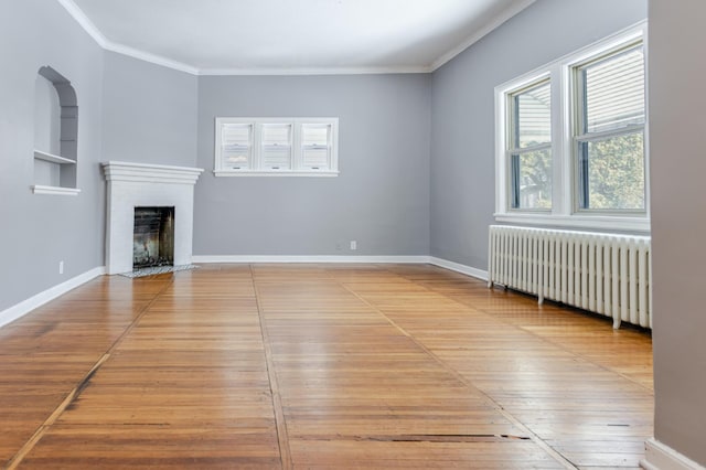 unfurnished living room featuring a brick fireplace, crown molding, baseboards, radiator heating unit, and wood finished floors