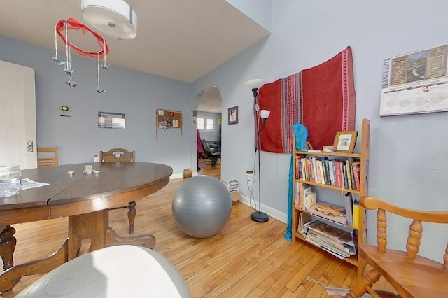 exercise room with arched walkways, vaulted ceiling, baseboards, and wood finished floors